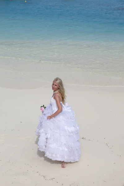 青いセによってビーチの砂の上に長い白い花嫁のドレスを着た若い美しい女性 — ストック写真
