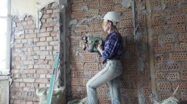 Çalışma kıyafetleri ve kırmızı tuğla kampları arka plan karşı puncher ile bir inşaat kask genç kadın, İnşaat işleri. Apartman yenileme