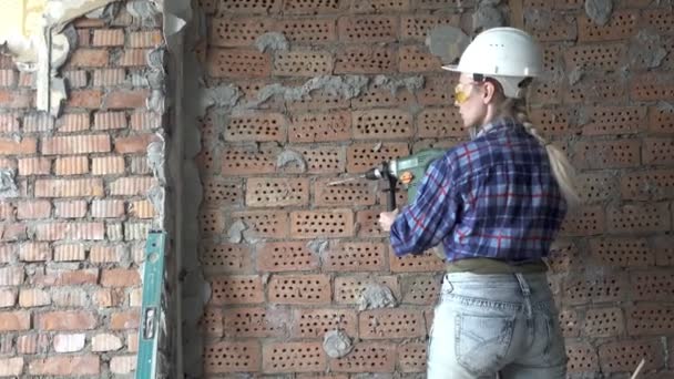Çalışma kıyafetleri ve kırmızı tuğla kampları arka plan karşı puncher ile bir inşaat kask genç kadın, İnşaat işleri. Apartman yenileme — Stok video