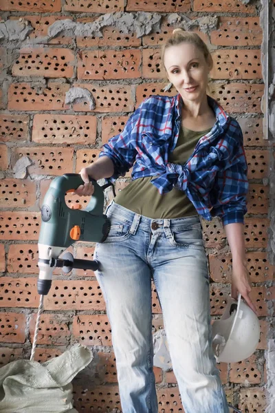 身着工作服 头戴防护头盔的年轻女子站在砖墙旁 手持重锤钻 — 图库照片