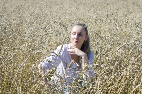 夏の日に金色の小麦の耳のフィールドに長いブロンドの髪を持つ白いブラウスの美しい若い女性の肖像画 — ストック写真