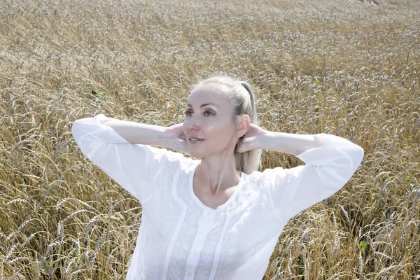 夏の日に金色の小麦の耳のフィールドに長いブロンドの髪を持つ白いブラウスの美しい若い女性の肖像画 — ストック写真