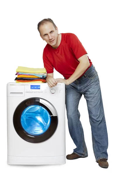 新しい洗濯機ときれいな洗濯物のスタックの隣に立って微笑む幸せな男 — ストック写真