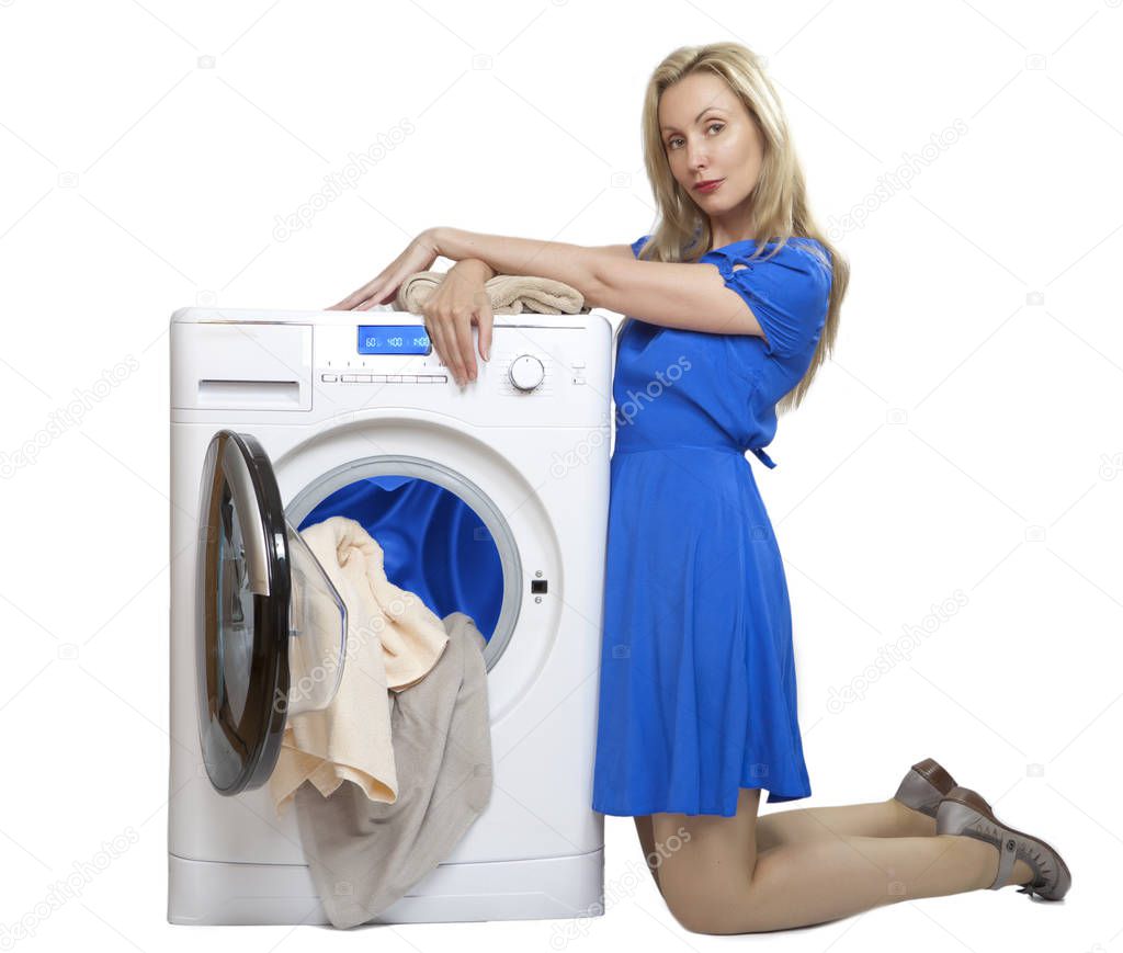 young woman in a blue dress kneeling unloads laundry from a new washing machine