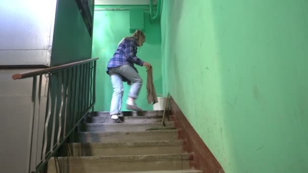 ブルージーンズとケージシャツを着た若い女性が階段の上で床をスイングし 洗うスターリン主義の建物のエレベーターの横にあるアパートの建物 労働移民の掃除による公共スペースの清掃 — ストック動画