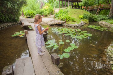 Zarif elbiseli küçük kız doğada göletler üzerinde ahşap köprüde yürür, bahar günü açık havada.