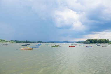 Fırtınalı bulutlu gökyüzü ile Tuna Nehri üzerinde renkli tekneler 