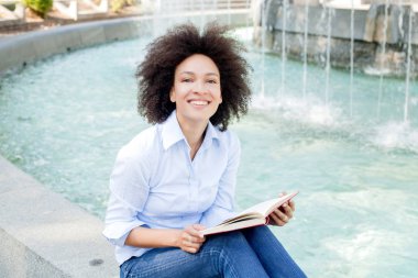 Güzel Afro Amerikalı genç kadın kitap okumak, çekici karışık yarış Çeşme açık rahatlatıcı kadın portresi kameraya, rahat kıyafet arıyorum