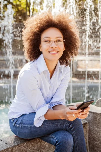 快乐的美国黑人年轻妇女与眼镜使用智能手机 户外人像混血女子 休闲装 看镜头 — 图库照片