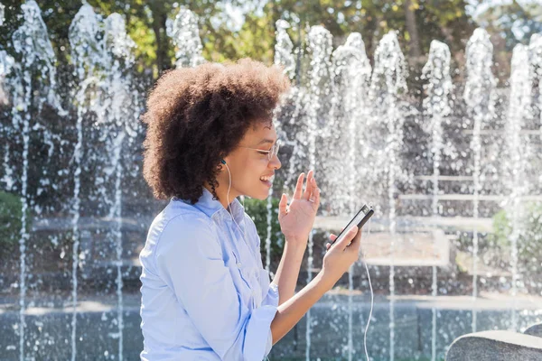 快乐年轻的非洲裔美国妇女在休闲服装 使用智能手机的社交网络 户外肖像 非洲卷曲的发型 看着电话 — 图库照片