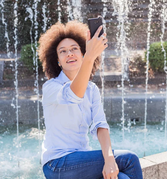 Atractiva Joven Afroamericana Feliz Desgaste Casual Sentada Cerca Fuente Escuchando —  Fotos de Stock