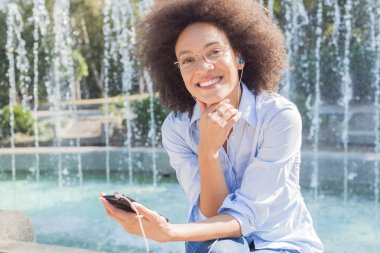 Kameraya bakarak telefon, giyim, açık portre kullanarak güzel mutlu genç yarış kadın kulaklık ile karışık