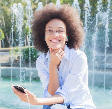 Kameraya bakarak telefon, giyim, açık portre kullanarak güzel mutlu genç yarış kadın kulaklık ile karışık