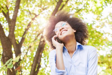Neşeli genç doğada telefonla konuşan kadın siyah. Açık portre, giyer gözlük, seyir vasıl belgili tanımlık yan, arka planda güneş ışığı Flare