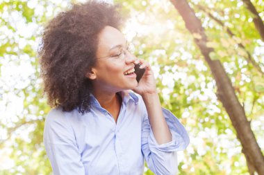 Neşeli genç telefonla konuşan kadın siyah. Açık portre, giyer gözlük, seyir vasıl belgili tanımlık yan, arka planda güneş ışığı Flare