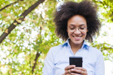 Telefonunuzun ve doğada güzel genç Afrikalı kadın. Açık portre seyir telefon gözlük, giyer