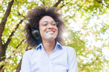 Güzel mutlu Afro Amerikalı genç kadın müzik dinlemek kulaklık doğada, çekici ile karışık portresi yarış eğlence açık 