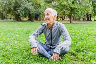 Kadın kıdemli dinlenmek doğa egzersiz sonrası parkta yeşil çimenlerin üzerinde oturan yaşlı kadın.