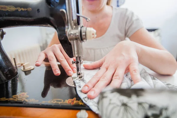 Closeup of female hands using retro sewing machine at home.