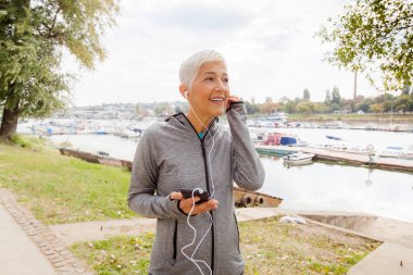 Nehri sahilinde, Olgun kadın egzersiz açık çalıştırdıktan sonra kadın kıdemli müzik dinlemek portresi.