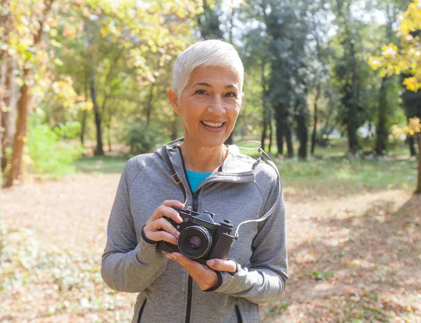 レトロなカメラの森で撮影の準備ができていると魅力的なシニア女性のポートレート — ストック写真