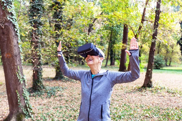 Happy Senior woman fun with virtual reality headset in forest, VR device using old people.
