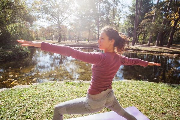 美丽的秋日清晨 年轻女子在湖边公园的垫子上练习瑜伽 — 图库照片