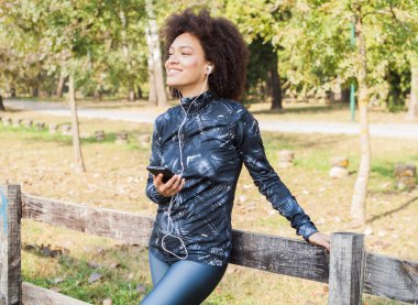 Çekici sportif kadın dinlenmek doğa ve yüzüne ahşap çit yaslanmış Park, müzik dinleme eğitimden sonra