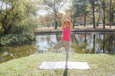 Genç kadın parkta tahta köprüde yoga egzersizi yapıyor. Dışarıda sağlıklı bir yaşam tarzı egzersizi..