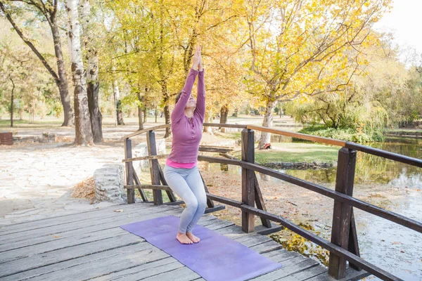 Woman Practicing Yoga , Doing Chair Exercise, On Wooden Bridge In The Park.