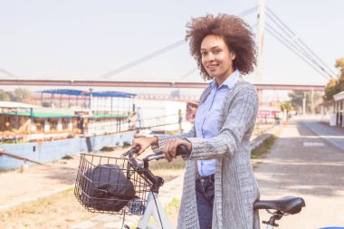 Mutlu ve güzel karışık ırk siyah kadın binmek bisiklet nehir kıyısında portresi.