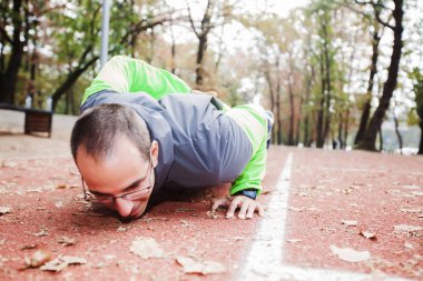Genç adam tek eliyle şınav çekiyor, gözlük takıyor, sonbahar sabahı açık hava spor parkında. Sağlıklı yaşam tarzı egzersizi.