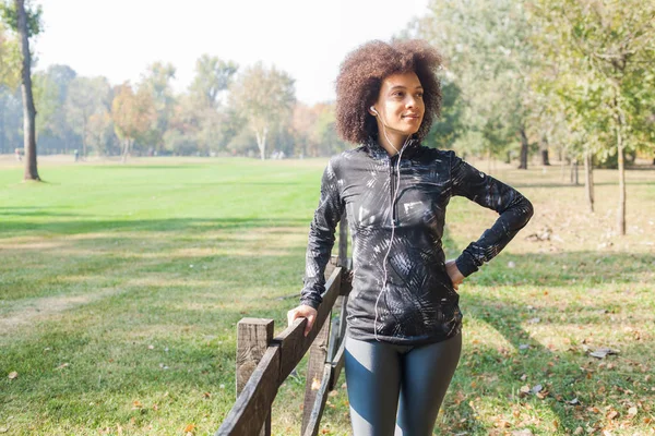 Çekici sportif kadın dinlenmek doğa ve yüzüne ahşap çit yaslanmış Park, müzik dinleme eğitimden sonra