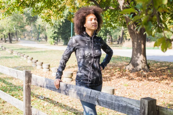 Çekici sportif kadın dinlenmek doğa ve yüzüne ahşap çit yaslanmış Park, müzik dinleme eğitimden sonra