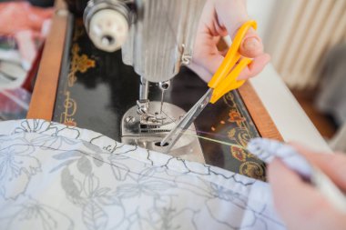Makas kullanarak ve retro dikiş makinesi üzerinde çalışan kadın terzi eller.