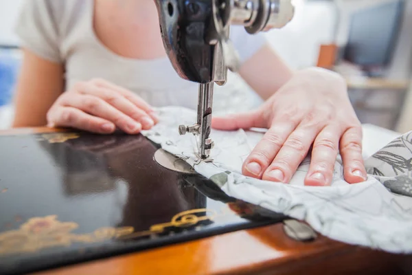 Female tailor hands using retro sewing machine for making dress at home.