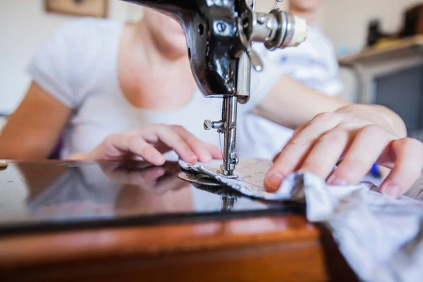 Female tailor hands using retro sewing machine for making dress at home.