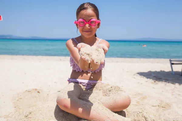 Kleines Mädchen mit Schwimmbrille hält am Strand Sand in den Händen — Stockfoto