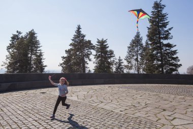 Küçük kız bahar günü parkta renkli uçan bir uçurtma tutuyor.