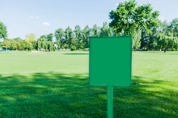 Empty sign board over green fields in the park at summer day