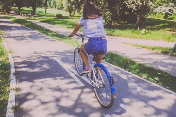 Bonita jovem mulher andar de bicicleta no parque vista traseira — Fotografia de Stock