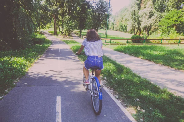 Bonita jovem mulher andar de bicicleta no parque vista traseira — Fotografia de Stock