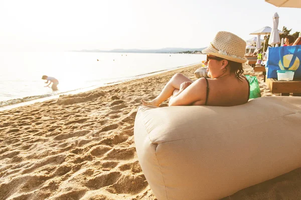 Mulher com chapéu de palha desfrutar do pôr do sol na praia perto do mar durante as férias de verão — Fotografia de Stock
