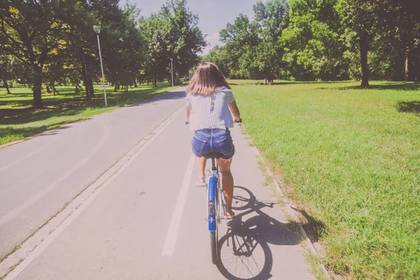 Hezká mladá žena jízda na kole v parku zadní pohled — Stock fotografie