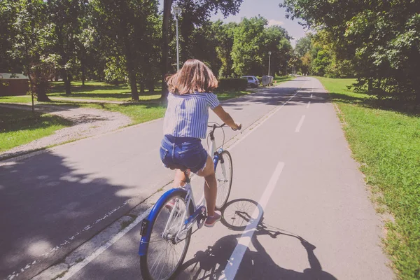 Bonita jovem mulher andar de bicicleta no parque vista traseira — Fotografia de Stock