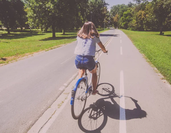 Bonita jovem mulher andar de bicicleta no parque vista traseira — Fotografia de Stock