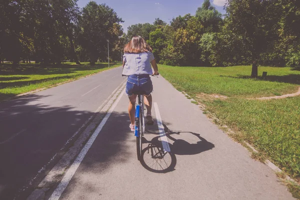 Όμορφη νεαρή γυναίκα καβάλημα ποδήλατο στο πάρκο πίσω όψη — Φωτογραφία Αρχείου