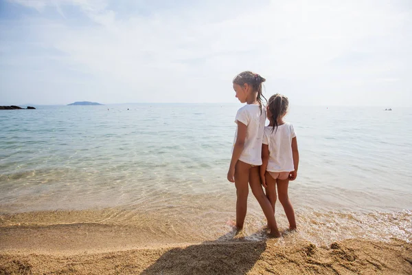 Dvě malé holčičky stojící spolu na písečné pláži — Stock fotografie