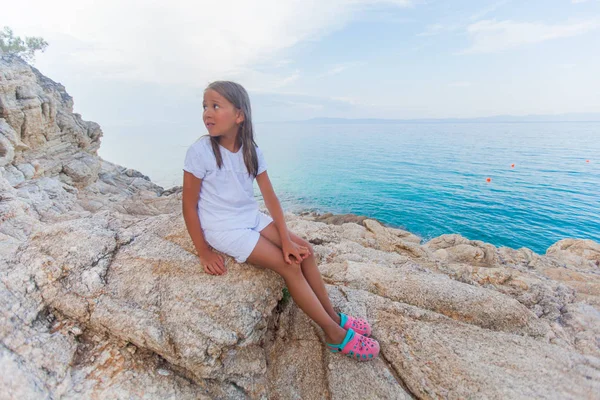 Cute little girl sitting on rocks shore — Stock Photo, Image