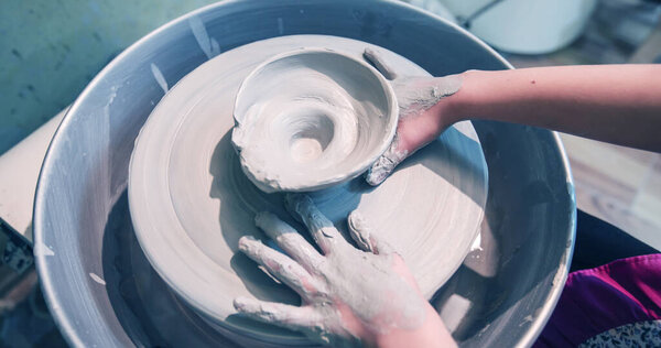 hands of young artist shaping clay on pottery wheel at workshop in ceramic studio